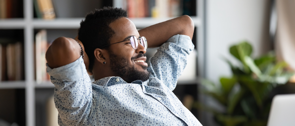 Smiling man relaxing with hands behind his head, sitting in a cozy home office.