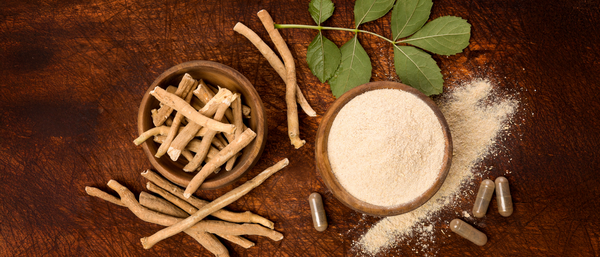 A collection of ashwagandha roots, powder, leaves, and capsules displayed on a rustic wooden surface.