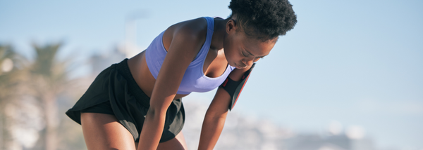 A woman in athletic wear leans forward with her hands on her knees, catching her breath.