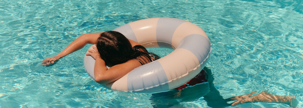 A person floats in a swimming pool on a pastel-striped inflatable ring, resting their head on the side.