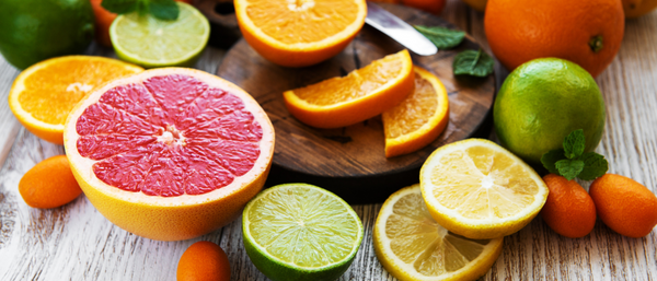 Sliced grapefruit, lime, lemon, and oranges arranged on a wooden table with kumquats and mint leaves.