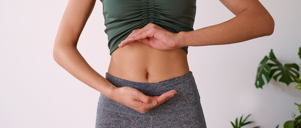 Close-up of a woman's midsection as she makes a hand gesture around her stomach, symbolizing gut health or digestion.