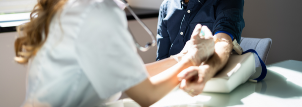 A medical professional in a white coat is drawing blood from a patient's arm using a syringe.